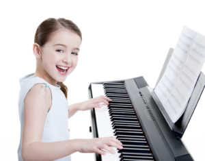 Cute happy smiling girl plays on the electric piano - isolated on white.